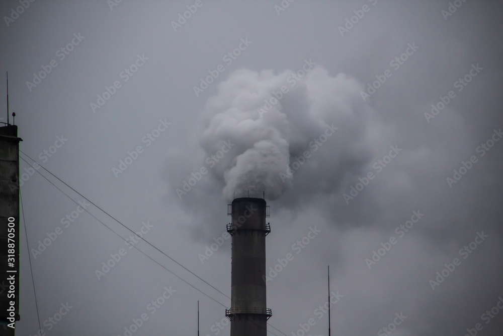 Industrial Smoke Pipe against grey sky. Industrial chimney fume mix in clouds. Smoke air emissions from pipe on a grey sky