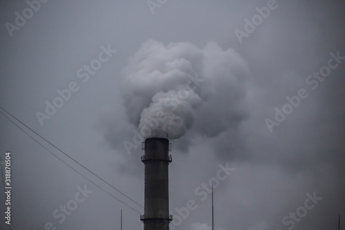 Industrial Smoke Pipe against grey sky. Industrial chimney fume mix in clouds. Smoke air emissions from pipe on a grey sky