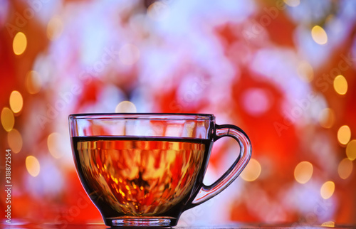 Transparent cup with black tea on a magical colorful background. The atmosphere of the holiday and cozy autumn.