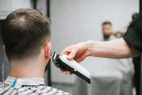 Barber's hand with a clipper cuts the back of a man's neck. Haircuts in barbershop. Hairdresser shaves a young man hair clipper. Men's haircuts in the man beauty salon. Background. Copy space