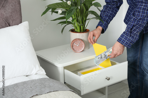 Man hiding dollar banknotes in cabinet indoors, closeup. Money savings
