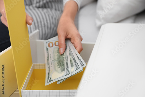 Fotografie Woman hiding dollar banknotes in box at home, closeup