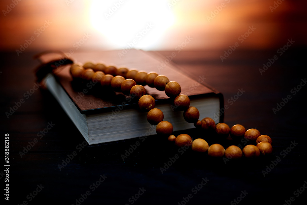 Bible and church rosary on a dark brown background with a radiance behind. Symbol of faith, religiosity, prayer. Bible and church rosary on a dark brown background with a radiance behind. Symbol of faith, religiosity, prayer.