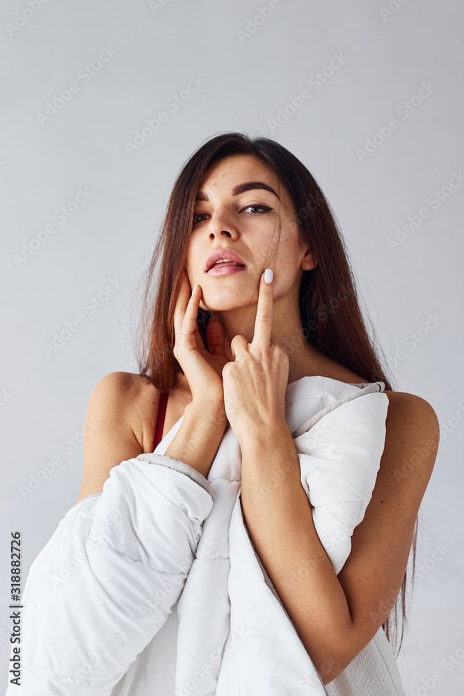 Touching face by hands. Woman covering her body by towel in the studio against white background Touching face by hands. Woman covering her body by towel in the studio against white background