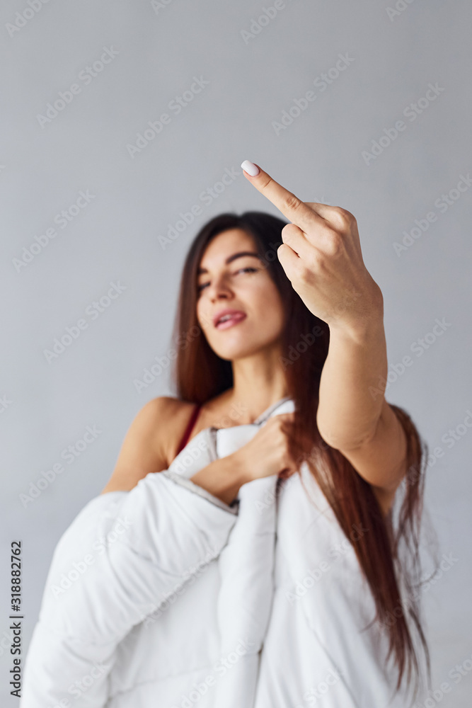 Woman with middle finger stands and covering her body by towel in the studio against white background Woman with middle finger stands and covering her body by towel in the studio against white background