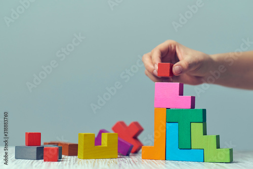 Hand holding piece of wooden block puzzle. wood cube stacking. Concept of complex and smart logical thinking. Slightly defocused and close up shot. on a red background