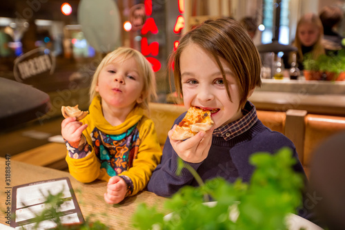 Happy european children, eating pizza at a restaurant, evening time