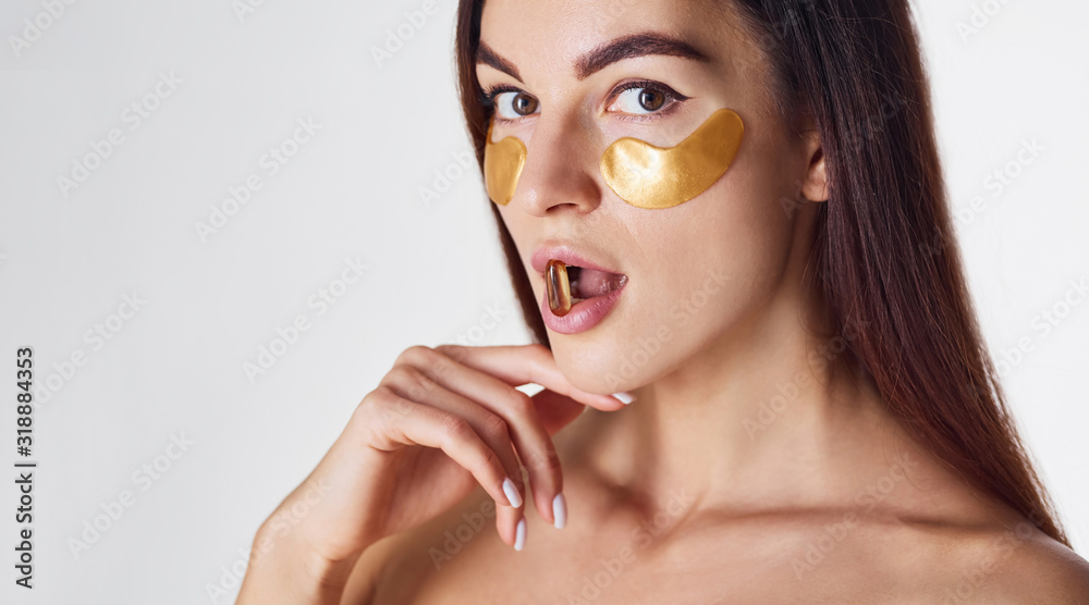 Naked woman in the studio with golden tapes near eyes and with pill in mouth Naked woman in the studio with golden tapes near eyes and with pill in mouth