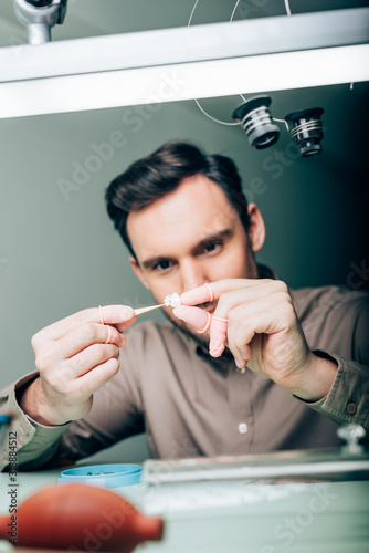 Selective focus of watchmaker working with watch part by equipment on table