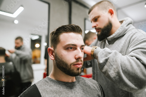 Creating a stylish men's hairstyle in a barbershop. Professional barber invests hair of handsome bearded man. Hair styling in men's hairdresser.