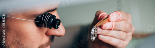 Panoramic shot of watchmaker in eyeglass loupe holding watch detail in tweezers