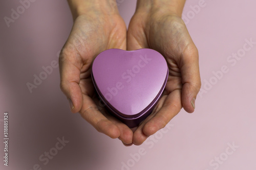 In female young hands lies a small heart-shaped box  close-up  on a light pinkish background.
