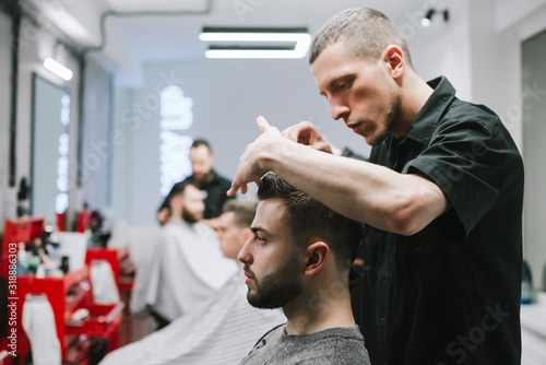 The concubine barber finishes the work of cutting a bearded man, invests hair with gel hands. Male hairdresser styling client's hair after haircut. Barbershop concept.