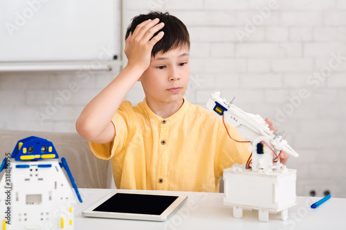 Schoolboy creating robot at class, making mistake photo