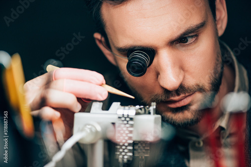 Selective focus of watchmaker working with wristwatch on timegrapher movement holder isolated on black photo