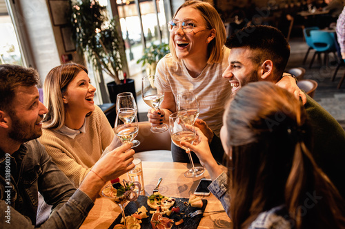 Group of young friends having fun in restaurant, talking and laughing while dining at table. 