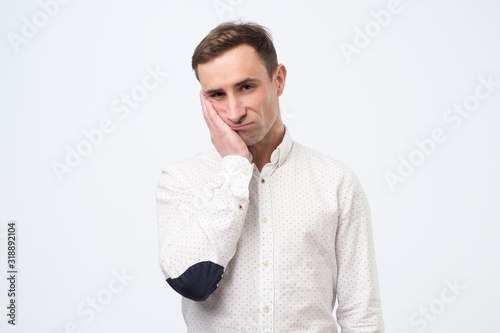 Very bored adult italian man holding hand on cheek looking tired and sick photo