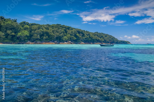 view of a long-tail boat floating in blue-green sea with green island and blue sky background, Tachai island, Mu Ko Similan National Park, Phang Nga, south of Thailand.