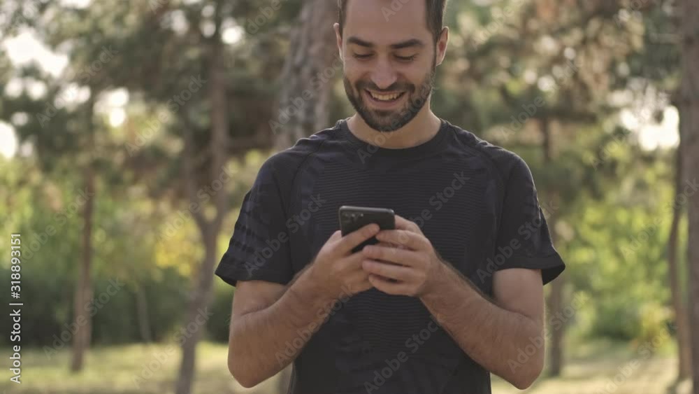 Happy handsome sportsman writing message on smartphone in park outdoors Happy handsome sportsman writing message on smartphone in park outdoors