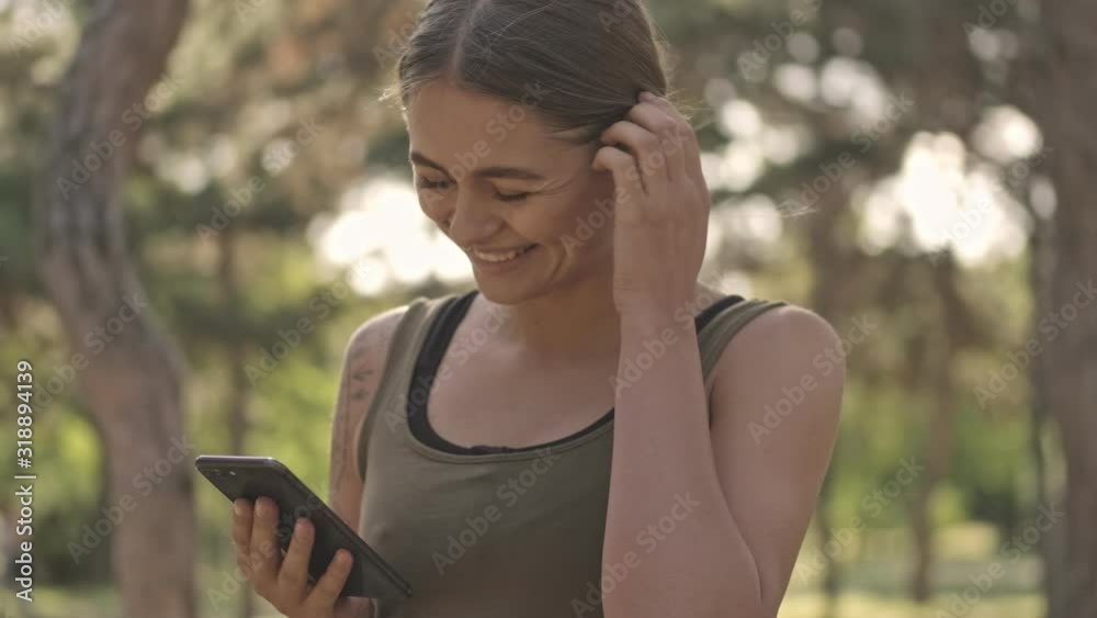 Cheerful young pretty sports woman using smartphone in park outdoors Cheerful young pretty sports woman using smartphone in park outdoors