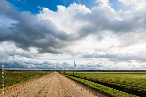 Storm clouds above the empty dirt road. Agricultural fields and forest in the background. Warm evening sunlight. Baltic sea, Garciems, Latvia photo