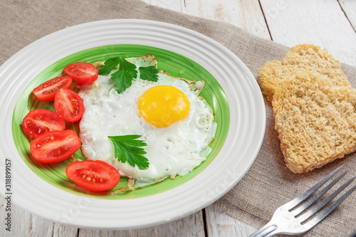 Fried eggs, heart shaped bread and red tomatoes on linen napkin on wooden background