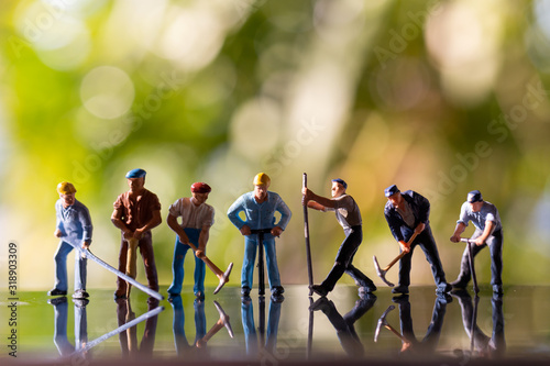 Miniature people worker holding tool outdoors with green bokeh background