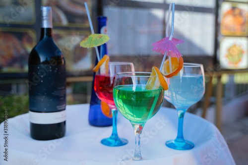 colorful cocktails with umbrellas and pieces of fruit are on the street on the table in a cafe in summertime  daylight