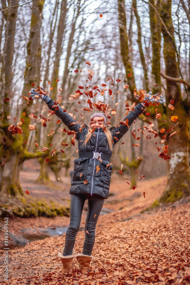 Fototapeta premium Blonde girl throwing red leaves in a beautiful forest