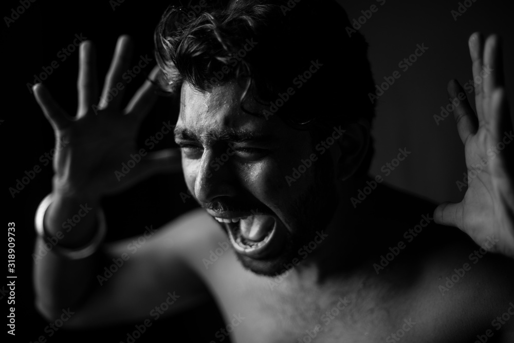 Monochrome portrait of young and handsome Indian Bengali brunette man in bare body crying loudly in black copy space background. Indian lifestyle and fashion photography