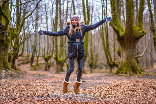 Blonde girl with hat jumping in a beautiful forest
