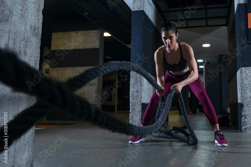 Fitness woman working out with battle ropes in the gym.