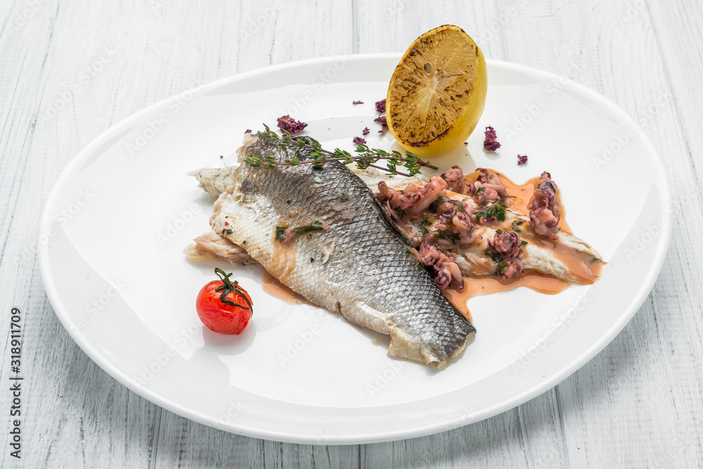 Baked sea bass with vegetables close up shoot on wooden background Baked sea bass with vegetables close up shoot on wooden background