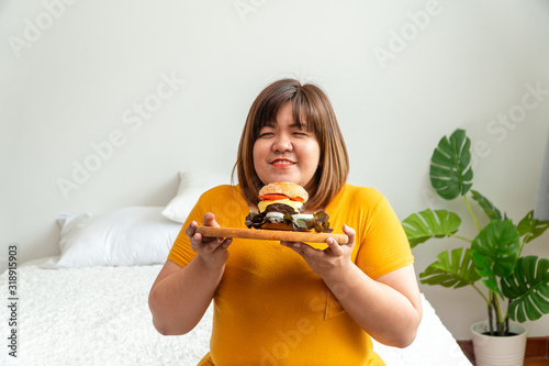 Obraz na plátně Hungry overweight young asian woman holding hamburger, Her hungry all time and overeat, gluttony and binge eating