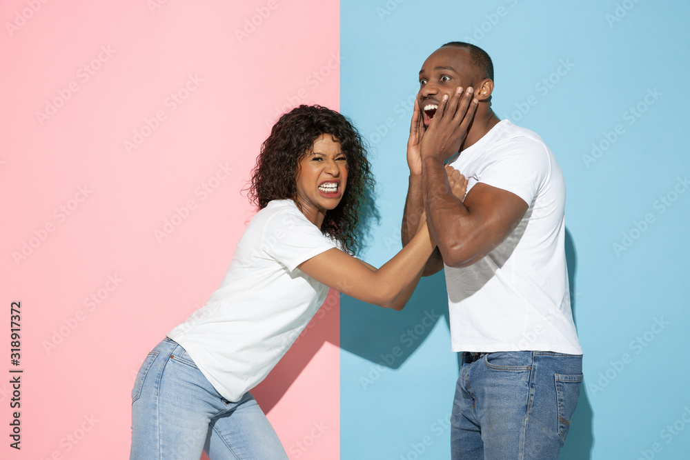 Fototapeta premium Screaming, angry. Young emotional man and woman in casual clothes on pink and blue bicolored background. Concept of human emotions, facial expession, relations, ad. Beautiful african-american couple.