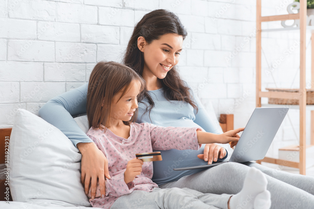 Pregnant mother and daughter shopping online, using laptop Pregnant mother and daughter shopping online, using laptop