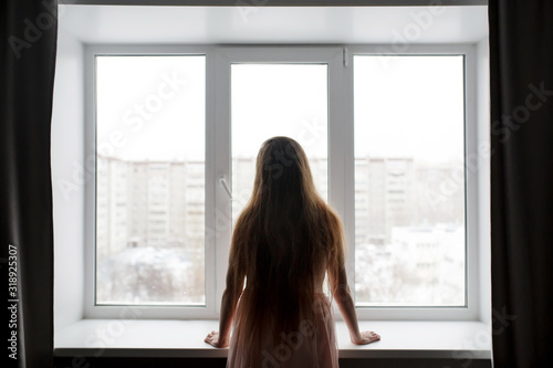 Rear view of woman silhouette standing near window looking out