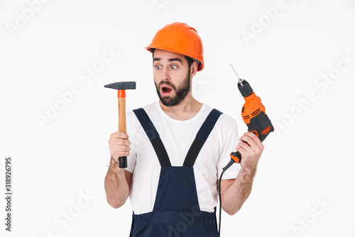 Shocked young man holding drill and hammer.