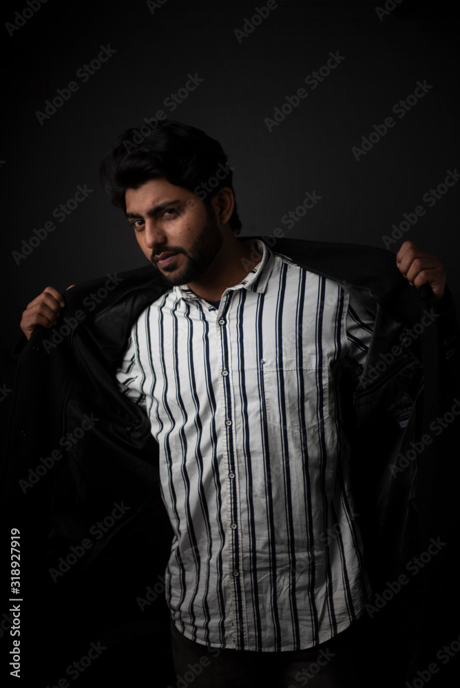 Fashion portrait of young and handsome Indian Bengali brunette man with striped formal shirt, black suit in black copy space background. Indian lifestyle and fashion photograph