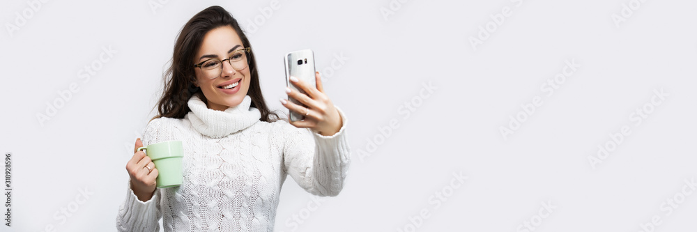 Portrait of a smiling casual beautiful woman using smartphone, taking selfie over white background. Banner crop for copy space Portrait of a smiling casual beautiful woman using smartphone, taking selfie over white background. Banner crop for copy space