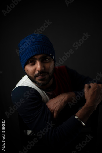 Fashion portrait of an young Indian Bengali brunette man in casual tee shirt and head band in black copy space background. Indian lifestyle and fashion photography.