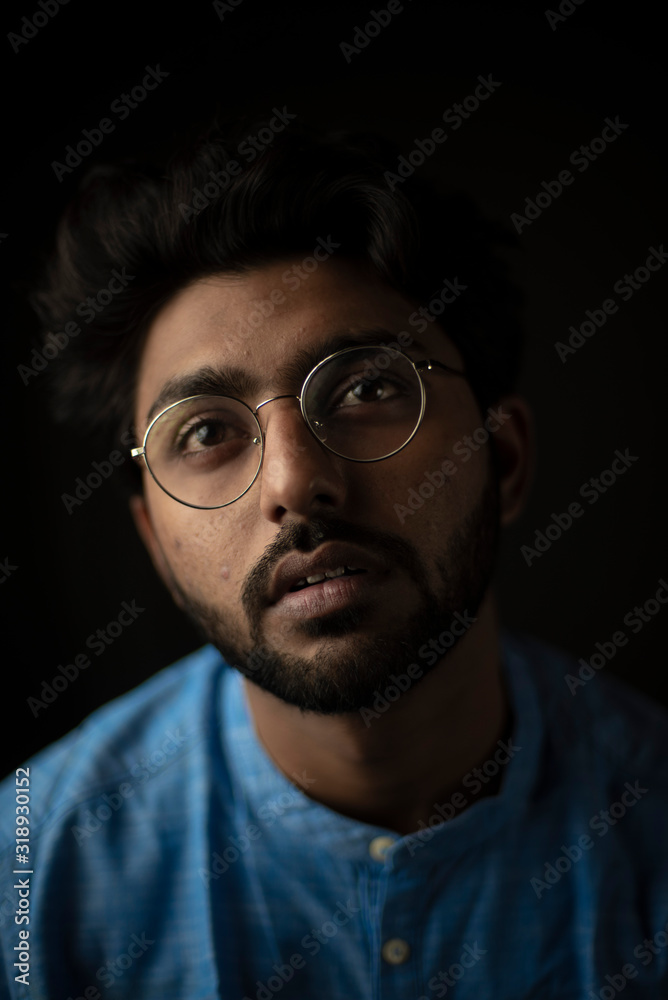 Obraz premium Fashion portrait of young and handsome Indian Bengali brunette man with traditional cotton wear and glasses in black copy space background. Indian lifestyle and fashion photography.