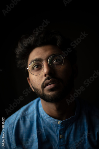 Fashion portrait of young and handsome Indian Bengali brunette man with traditional cotton wear and glasses in black copy space background. Indian lifestyle and fashion photography.