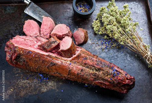 Barbecued dry aged venison tenderloin fillet steak and saddle natural with herbs offered as top view on a rustic metal tray
