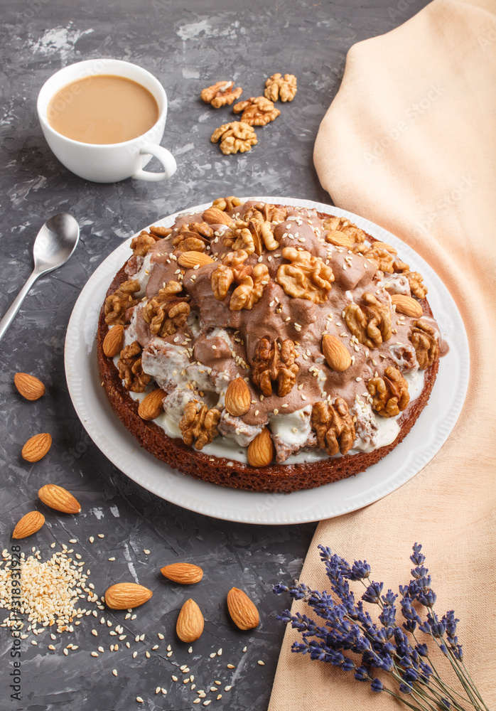 Homemade cake with milk cream, cocoa, almond, hazelnut on a black concrete  background with orange textile and a cup of coffee. Side view.