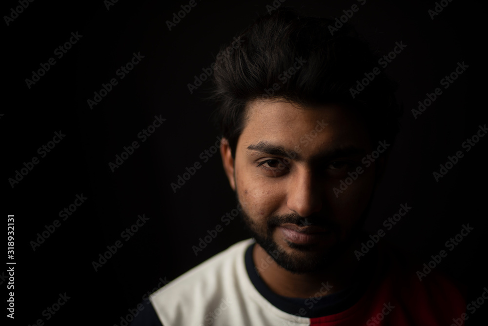 Fashion portrait of young and handsome Indian Bengali brunette man with casual tee shirt showing facial expression in black copy space background. Indian lifestyle and fashion photography