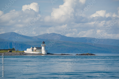 Seascape with lighthouse and mountan range far away. Hebrides islands, Scotland.