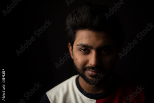 Fashion portrait of young and handsome Indian Bengali brunette man with casual tee shirt showing facial expression in black copy space background. Indian lifestyle and fashion photography