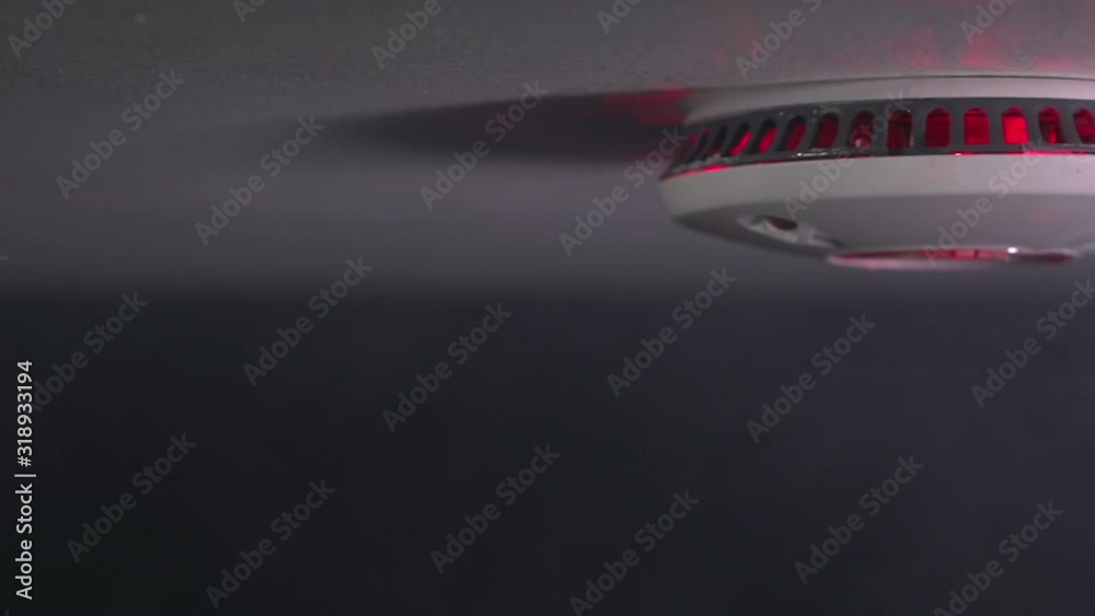 Smoke alarm detector with smoke rising - The light is flashing as there is a fire. Tracking shot