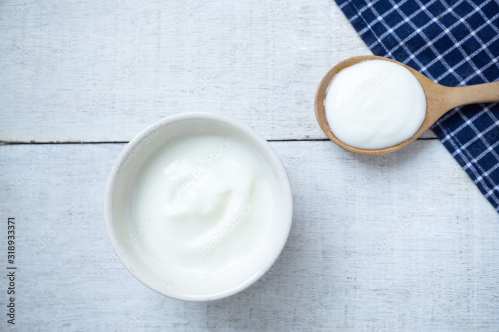 Natural white yogurt on white cup with wooden spoon on white wooden table.Top view. Natural white yogurt on white cup with wooden spoon on white wooden table.Top view.